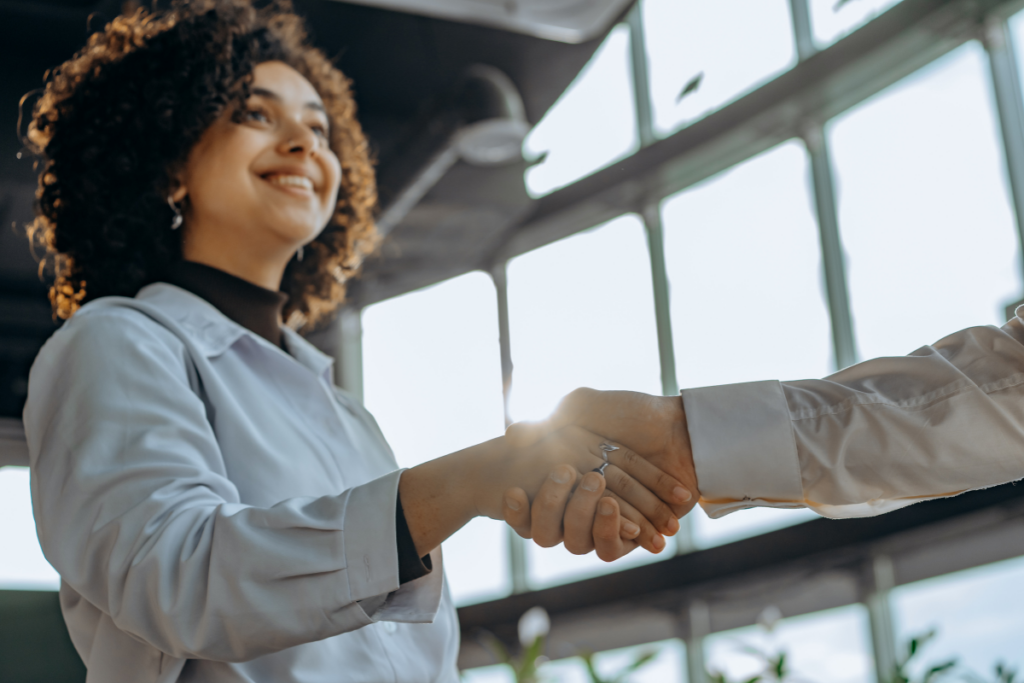 Two people smiling and shaking hands in a bright office, representing mentorship and partnership
